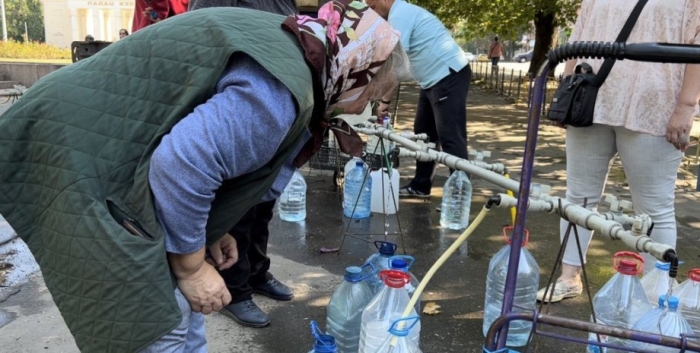 Бабуся набирає воду у пляшки